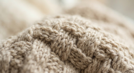 Close-up macro shot of minimalist beige knit sweater texture with soft natural studio lighting and intricate yarn weaving generated via generative model